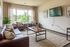 Inviting living room with modern leather sofas, large windows with scenic views, and a wall-mounted TV. Neutral decor, lush greenery, and abundant natural light create a welcoming atmosphere.