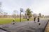 Vibrant outdoor basketball court scene with four people enjoying a friendly game under clear skies, surrounded by lush greenery.