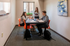 Bright study room with modern furniture featuring three people collaborating at a sleek table with vibrant orange chairs.