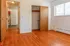 Bright, spacious room with hardwood floors, open closet, and large window, leading to a cozy kitchen.