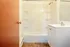 Bright and inviting bathroom featuring a modern shower-tub combo, sleek white vanity, and warm-toned door.