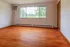 Bright and spacious room with polished wooden floors, large window with lush green views, and cozy natural lighting.