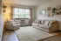Bright and cozy living room with a large window, plush beige sofas, soft area rug, and elegant wall art, creating a serene and inviting atmosphere.