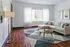 Bright and elegant living room featuring a cozy beige sectional sofa, modern art, and floor-to-ceiling windows with sheer curtains. A geometric rug and round wooden coffee table add charm.
