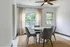Bright dining area with modern furniture, featuring a round table and four cushioned chairs, complemented by a woven rug and large window with light curtains.