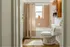 Charming bathroom featuring a cozy tub with pink tile, wooden cabinets, and a sunlit window with a potted plant.