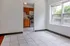 Bright living room with tiled flooring and a view into a cozy kitchen featuring wooden cabinets and modern appliances.
