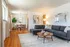 Bright and inviting living-dining area featuring a cozy gray sectional, vibrant greenery, and stylish decor under warm natural lighting.