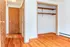 Bright hallway leading to a spacious wooden open closet, featuring polished hardwood floors and warm wooden doors.