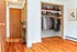Charming apartment hallway showcasing warm wooden floors, an organized open closet with stylish clothing, and tasteful decor.