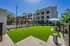 Modern apartment complex with vibrant green lawn, stylish outdoor seating, and shaded cabanas under a clear blue sky.