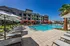 Modern apartment complex with luxurious pool area, vibrant orange cabanas, and stylish lounge chairs under sunny blue skies.