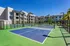 Modern apartment complex with luxurious tennis courts surrounded by lush greenery and clear blue skies.