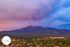 Breathtaking aerial view of lush green landscape and majestic mountains under a vibrant, colorful sky at sunset, with cozy cottages nestled in a peaceful community.