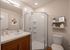 Modern bathroom featuring a sleek glass shower, stylish vanity with elegant countertop, and chic wall decor. Shelves with minimalistic accessories enhance the space.