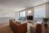 Bright and inviting living room with modern decor, featuring plush leather sofas, stylish art pieces, and a spacious balcony view.