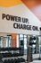 Invigorating fitness center with motivational 'Power Up. Charge On.' mural, featuring state-of-the-art weightlifting equipment and bright, energizing decor.