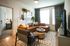 Cozy and modern living room with stylish decor, featuring a brown sectional sofa, chic armchair, and natural light through large windows.