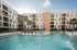 Modern apartment complex featuring a luxurious outdoor swimming pool with elegant lounge chairs, surrounded by palm trees and contemporary architecture.