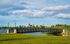 Breathtaking view of a serene park with a charming bridge, lush greenery, and city skyline in the background under a vibrant blue sky.