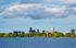 Breathtaking city skyline view over a serene lake surrounded by lush greenery under a vibrant sky.
