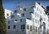 Modern multi-story apartment building with stylish balconies and rooftop space, set against a clear blue sky.
