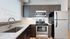 Modern kitchen with sleek stainless-steel appliances, including a refrigerator and oven, dark wood cabinetry, and a large sink under bright natural lighting.