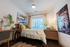 Cozy bedroom with modern decor, featuring a large window for natural light, stylish artwork, and a comfortable bed with colorful pillows.