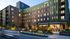 Modern urban apartment building with green and brick façade, vibrant community space, and bustling café entrance.
