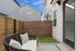 Charming outdoor patio with a cozy seating area, elegant cushion design, wooden privacy fence, and serene blue sky backdrop.