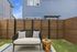 Charming outdoor patio with a cozy bench, decorative pillows, unique wooden side table, and privacy fence in a tranquil backyard setting.