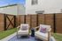 Charming outdoor patio space featuring cozy seating with plush cushions, fresh greenery, and a contemporary wooden fence.