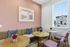 Charming corner nook with wicker seating, decorative pillows, and elegant brass tables with vibrant floral accents, set against a warm blush wall and a bright window view.