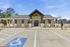 Inviting single-story building with modern stone accents, ample parking, and scenic green surroundings under a bright blue sky.