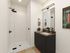 Elegant bathroom with a sleek glass-enclosed shower, modern dark vanity, and stylish lighting, creating a luxurious and inviting atmosphere.