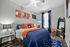 Vibrant bedroom design with modern decor, featuring a cozy bed adorned with orange and blue accents, stylish wall art, sleek nightstand, and large window draped in elegant curtains.