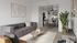 Modern living room with a sleek gray sofa, stylish decor, and open layout leading to a dining area and contemporary kitchen.