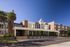 Modern brick apartment building with sleek design, surrounded by lush palm trees and a clear blue sky.