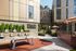 Modern urban courtyard featuring a ping pong table, stylish seating, vibrant greenery, and contemporary apartment buildings.