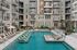 Luxurious apartment complex featuring a pristine pool with elegant lounging chairs, surrounded by stylish multi-story balconies and tropical landscaping.