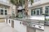 Modern outdoor kitchen area with sleek stainless steel grills, surrounded by lush palm trees and contemporary stone architecture.