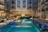Luxurious apartment courtyard featuring a modern swimming pool with stylish lounge chairs, ambient lighting, and elegant building facade.