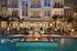 Luxurious apartment complex with a stunning pool, elegant lounge chairs, and ambient fire pits set against modern architecture and palm trees.