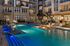 Luxurious apartment complex at night showcasing a sparkling pool with stylish fire features and elegant balconies.