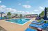 Inviting outdoor pool area with vibrant loungers and umbrellas, set against picturesque residential cottages and a sunny blue sky.