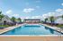 Luxurious outdoor pool area with plush lounge chairs and vibrant sunbeds, surrounded by modern cottages and lush greenery under a bright blue sky.