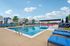 Modern outdoor pool area with vibrant lounge chairs and umbrellas, surrounded by charming suburban homes under a clear blue sky.