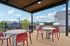 Chic outdoor patio with modern tables, red chairs, and a grill, offering a serene view of a tranquil suburban neighborhood.