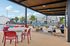 Modern outdoor patio area featuring stylish seating, a vibrant poolside view, and cozy shaded spaces under a wooden pergola, perfect for relaxation and gatherings.