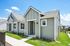 Charming single-story home with modern gray exterior, inviting porch, and lush green landscaping under a bright blue sky.